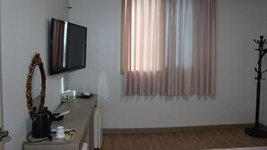 Una habitación con una televisión de pantalla plana montada en la pared, un escritorio de madera con un hervidor, una taza y una caja de pañuelos.