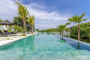 A clear infinity pool with lounge chairs and umbrellas, surrounded by palm trees and greenery. - Villa Kusuma (Pecatu)