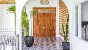 Un passadís amb un paviment estampat, una porta de fusta i plantes en testos.