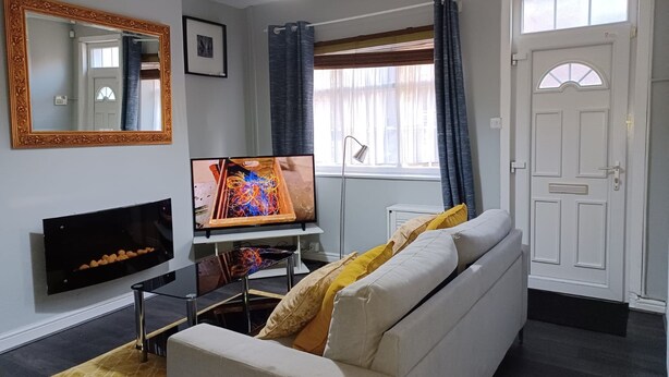 Una sala de estar con un sofá, un televisor de pantalla plana, un espejo y una puerta.