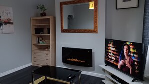 Una sala de estar moderna con televisor de pantalla plana, una estantería de madera, chimenea y un espejo grande.