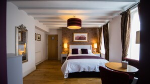 A hotel room with a large bed, two bedside tables with lamps, a round table with a chair, and a large mirror on the wall. - The Grove Hotel (Haverfordwest)