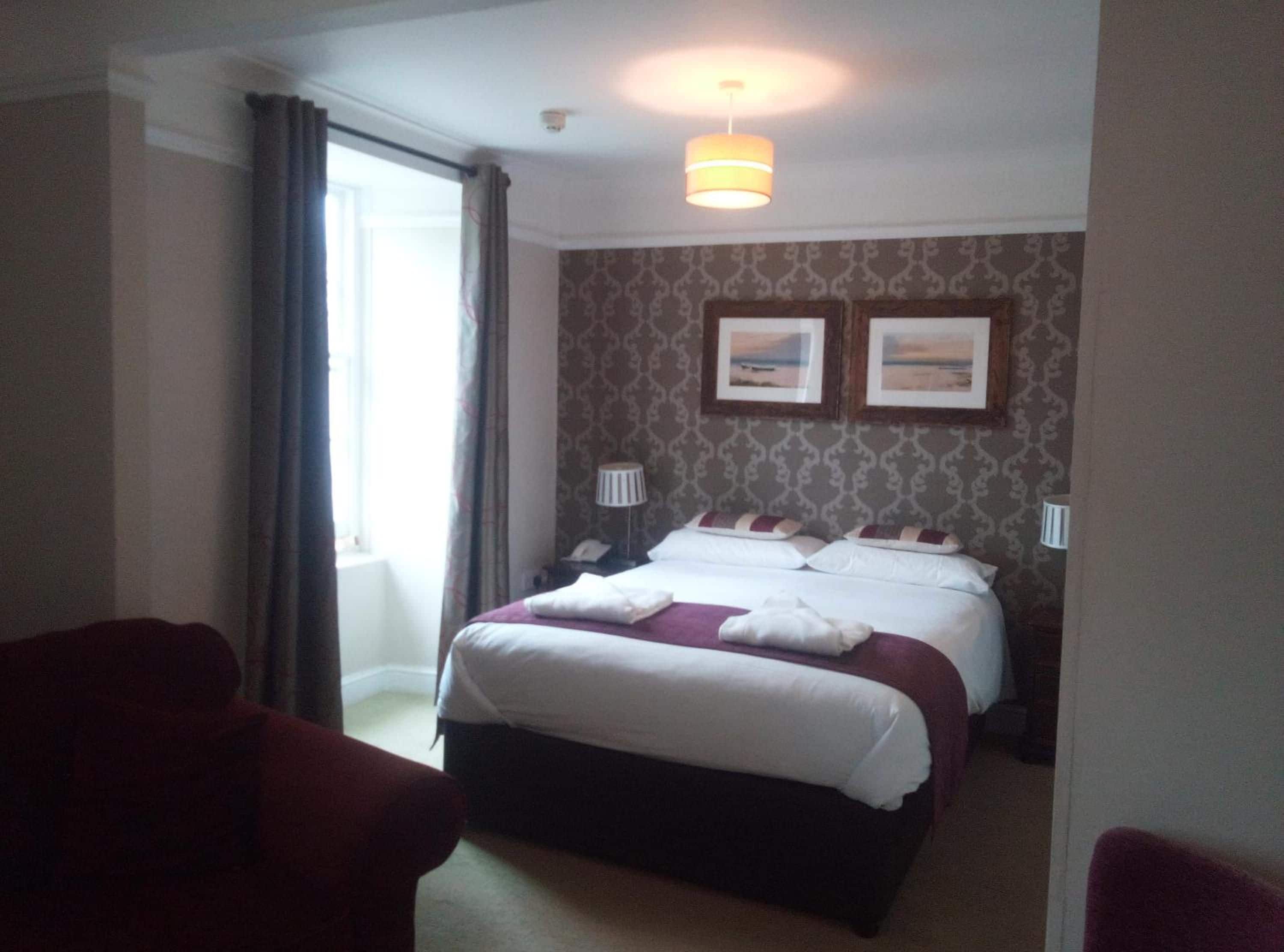Una habitación de hotel con una cama, dos lámparas de noche, un ventanal con cortinas y un cuadro colgado en la pared.