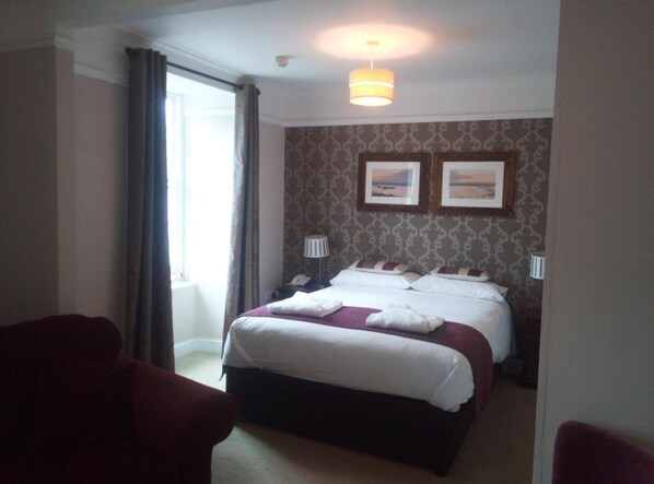 A hotel room with a bed, two bedside lamps, a window with curtains, and a wall-mounted picture. - The Grove Hotel (Haverfordwest)
