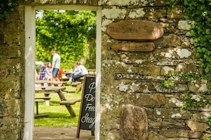 An entrance to a garden with a wooden sign that reads 'The Secret Garden Welcome.'