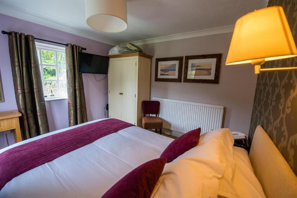 Een hotelkamer met een bed, een stoel, een kledingkast, een radiator en twee foto's in lijsten aan de muur.