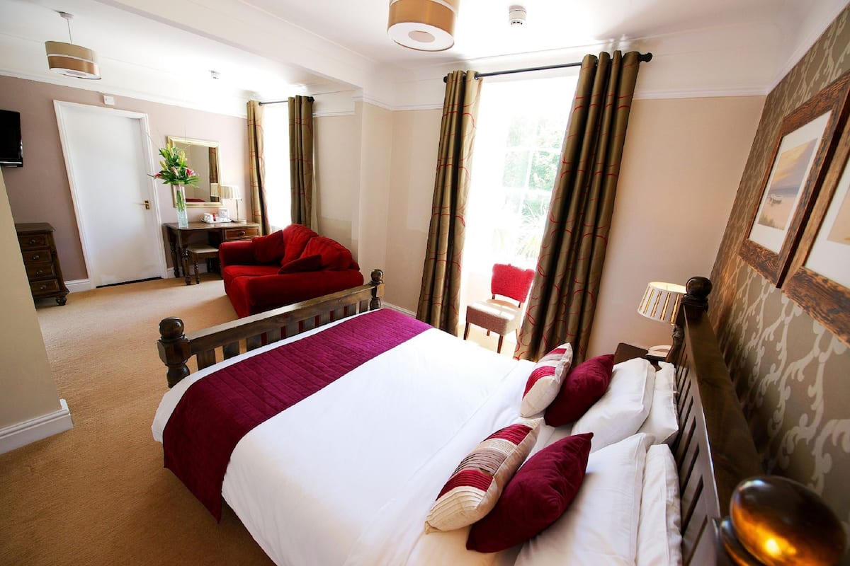 A hotel room with a large bed, red armchair, and a desk with a chair.