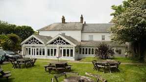 A white building with a large windowed porch, surrounded by a grassy lawn with multiple wooden tables and chairs. - The Grove Hotel (Haverfordwest)