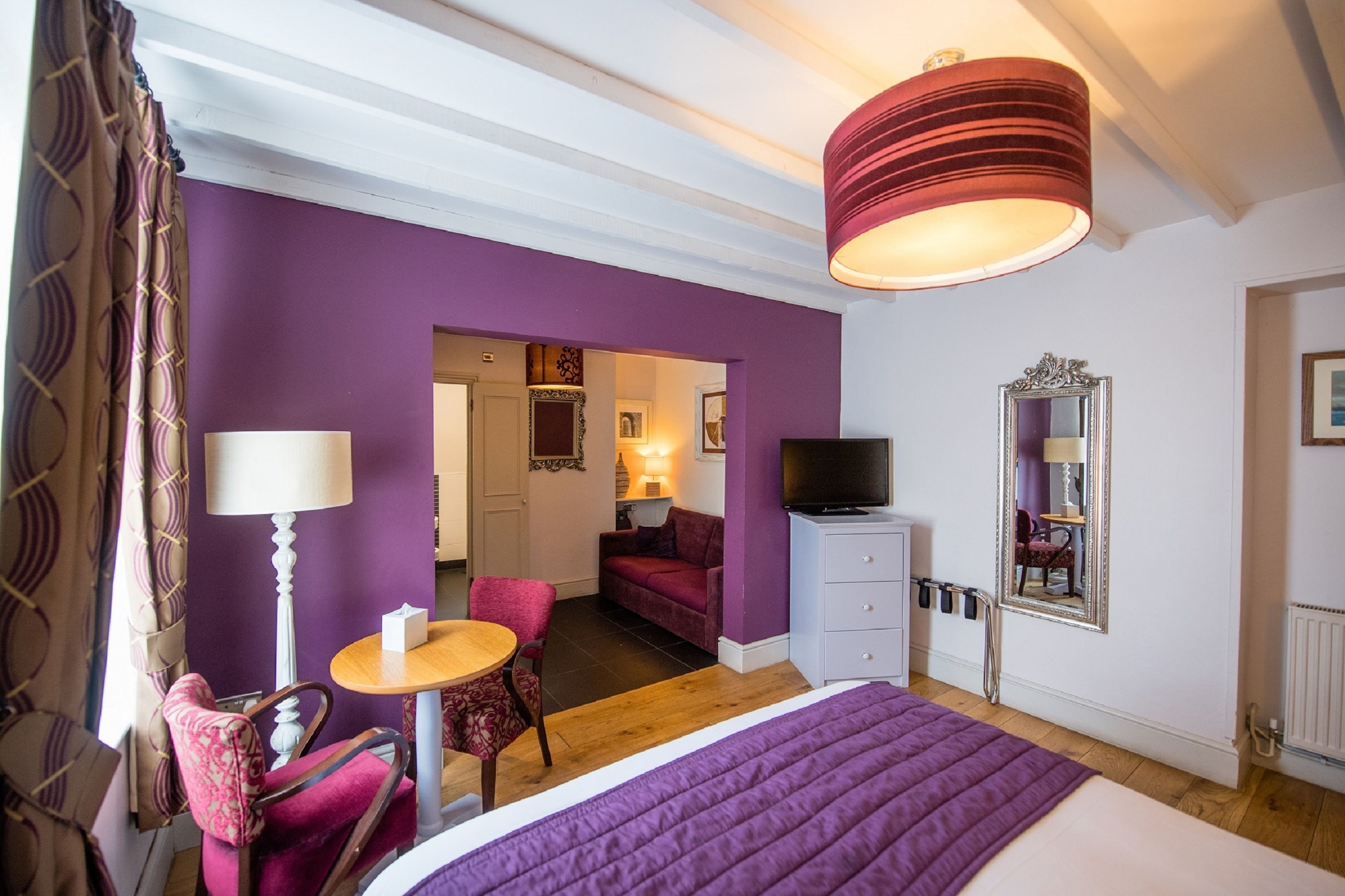 A bedroom with a bed, a TV, a desk, and a chair. There is a door leading to another room.