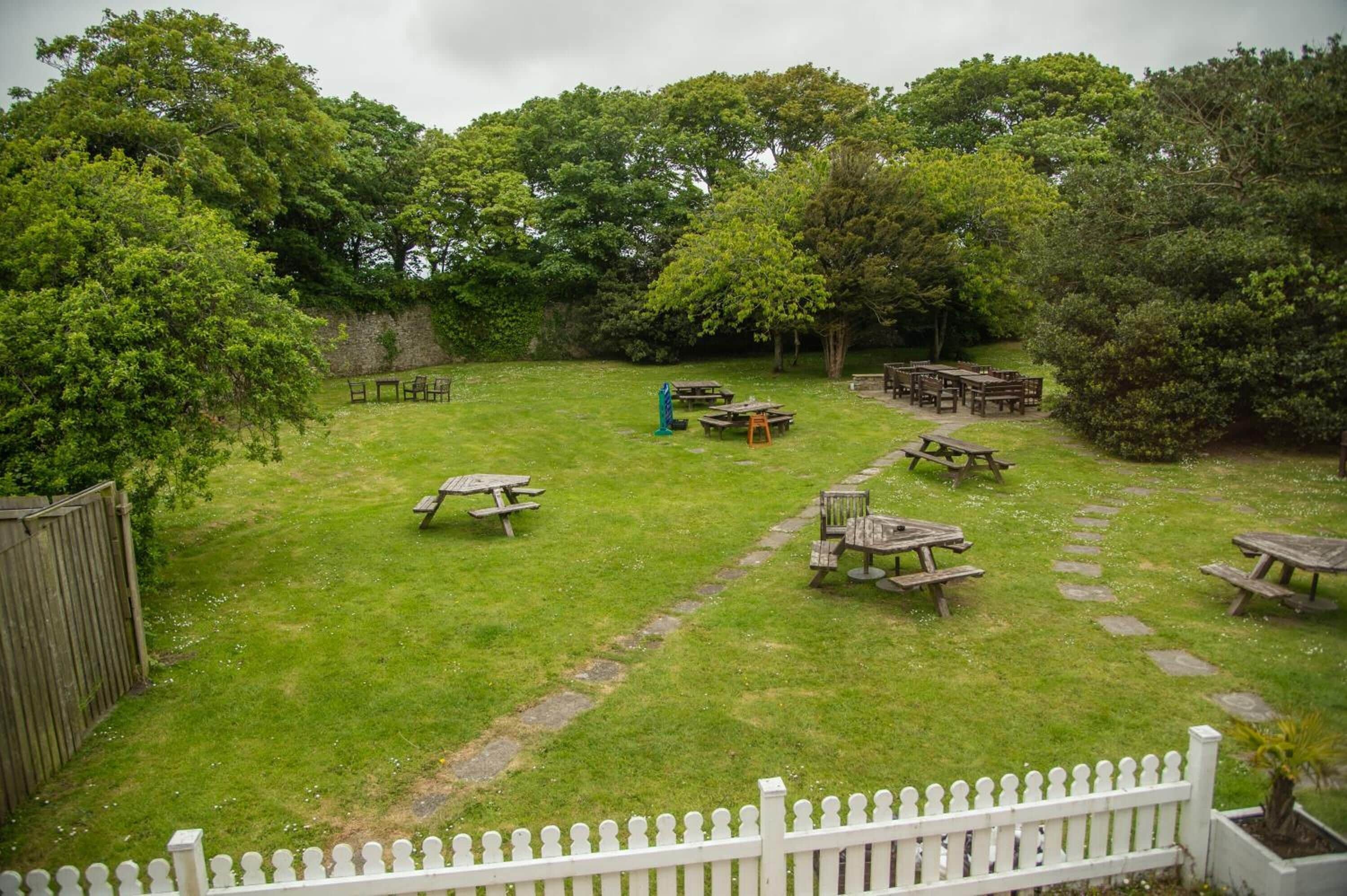 A grassy outdoor area with picnic tables and a white picket fence.