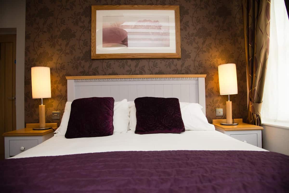 A hotel room with a large bed, two nightstands, a framed picture on the wall, and a window with curtains.