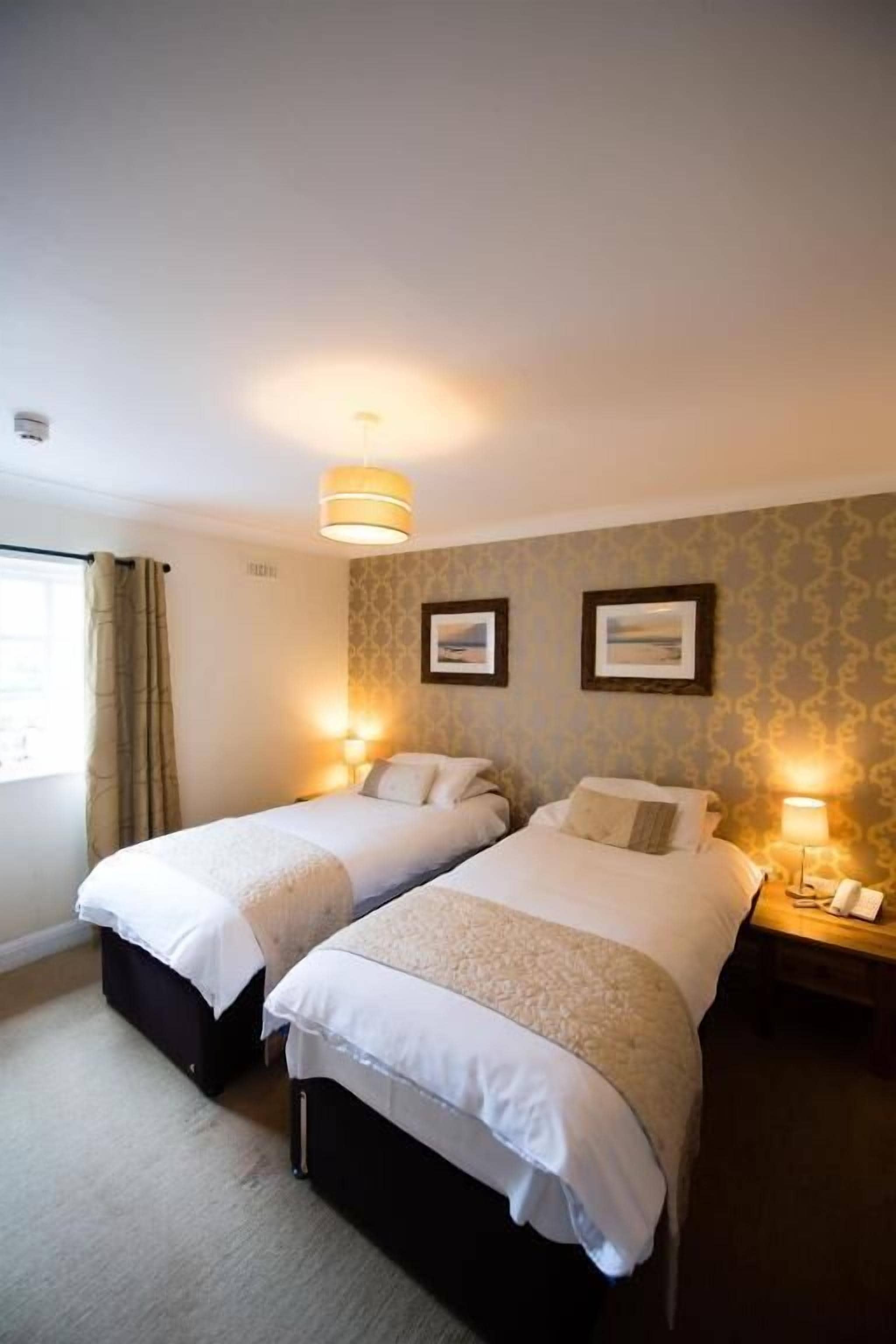 A hotel room with two single beds, a bedside table with a lamp, and a window with curtains.