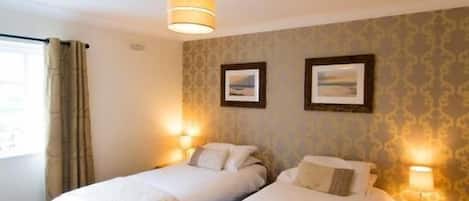 A hotel room with two single beds, a bedside table with a lamp, and a window with curtains.