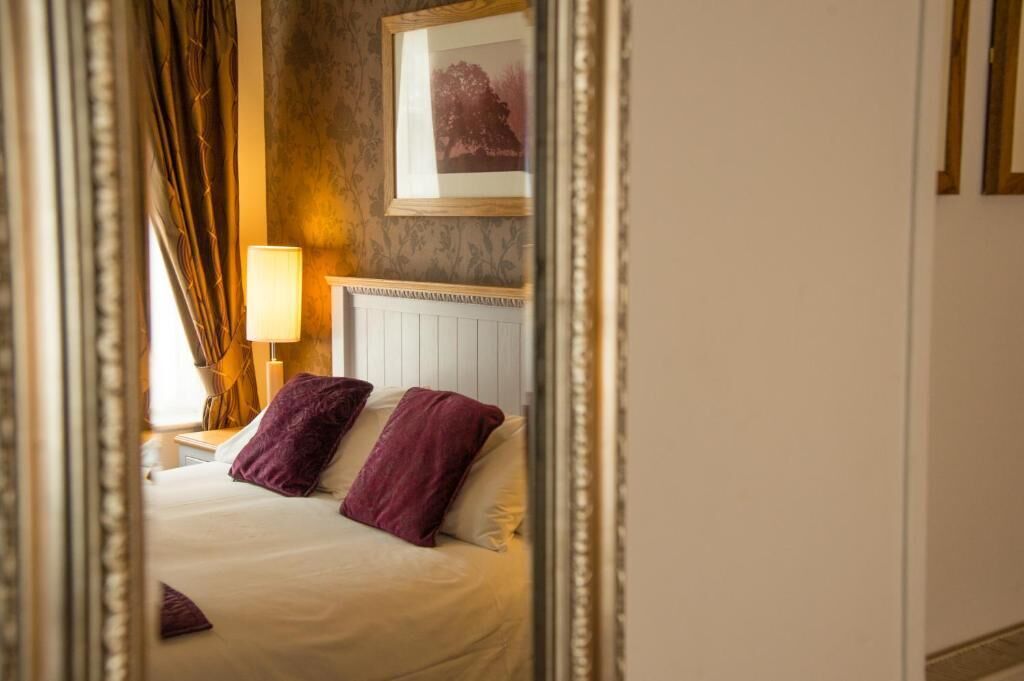 A hotel room with a bed, a nightstand, a lamp, and a framed picture on the wall.
