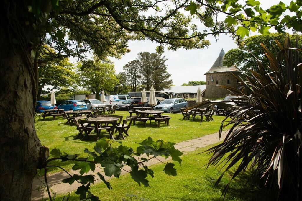 An outdoor seating area with picnic tables, surrounded by parked cars and a building with a conical roof.