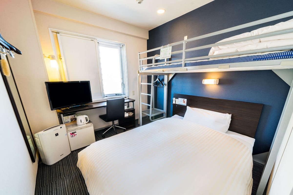 Et hotelværelse med køjeseng, et skrivebord med computer, et fjernsyn, et minikøleskab og et lille siddeområde.