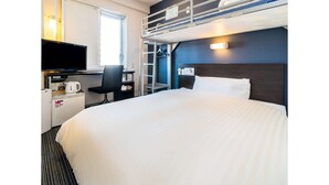 Hotellihuone, jossa on kerrossänky, työpöytä tietokoneella, tuoli, valkoisilla lakanoilla varustettu sänky ja televisio.