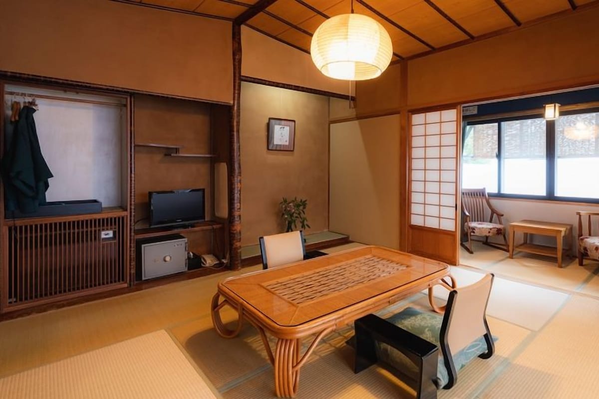 A traditional Japanese room with tatami flooring, a low table, chairs, a television, and sliding doors.