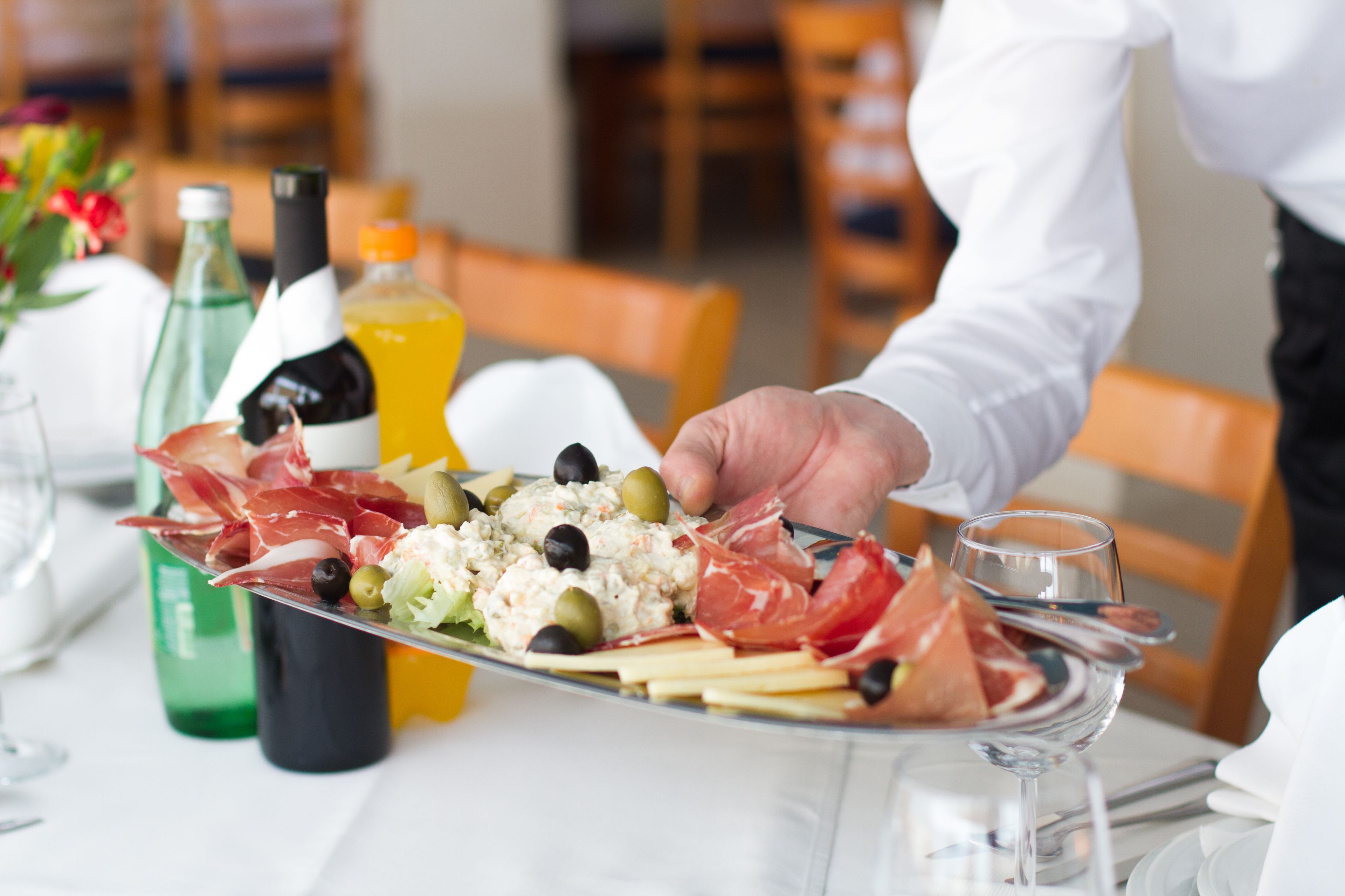 A person serving a platter of food including olives, cheese, and cured meats.