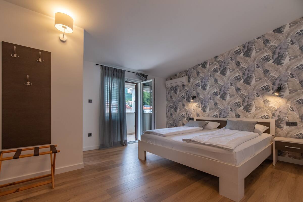 Un dormitorio con una cama grande, un banco de madera, un aire acondicionado de pared y vistas a través de un ventanal.