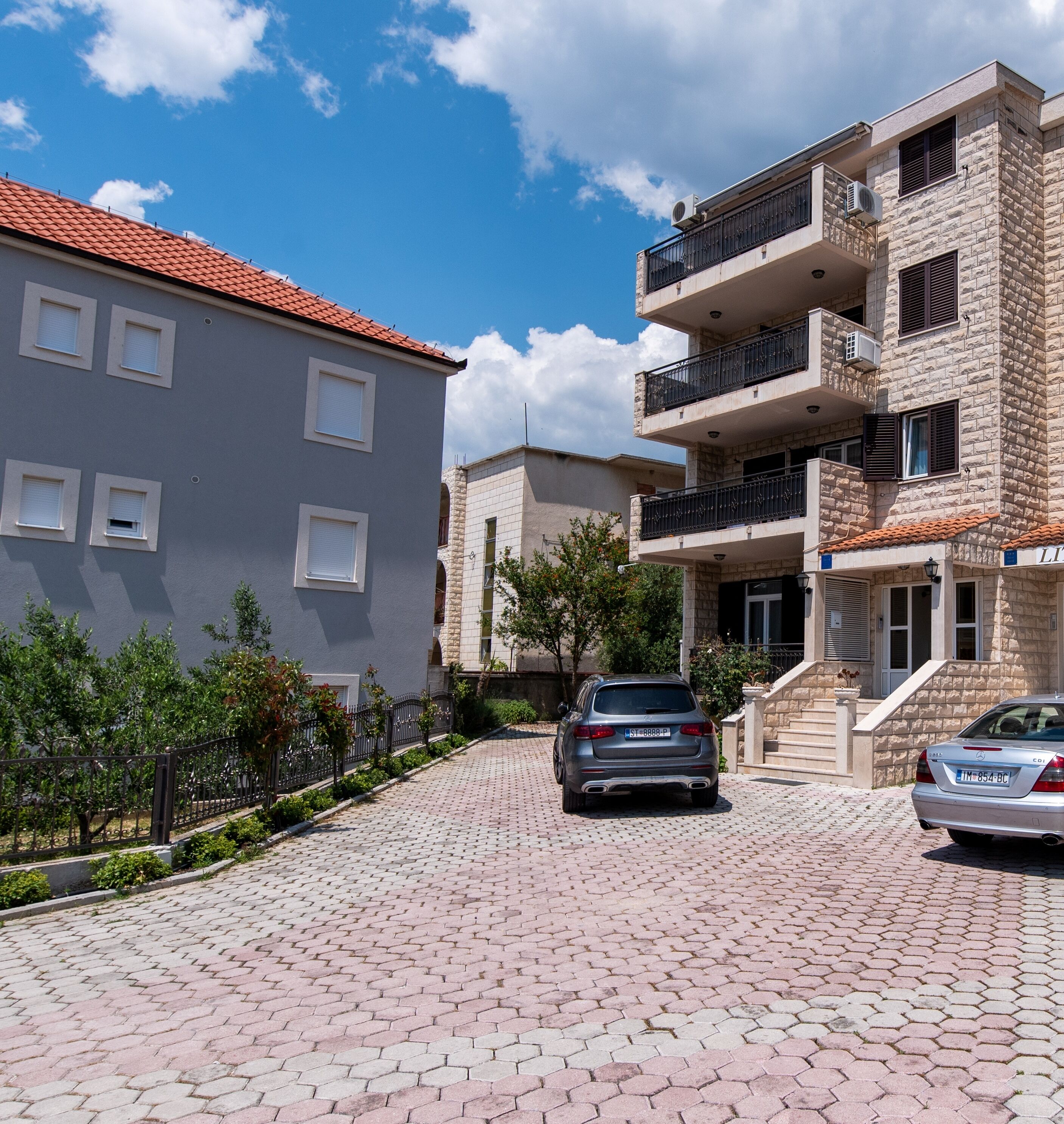 A residential street with two-story buildings, a paved driveway, and parked cars.