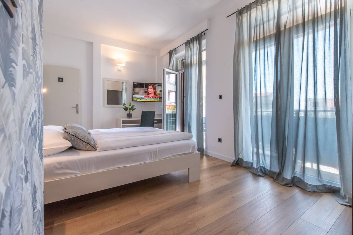Un dormitorio moderno con cama, televisor y balcón con cortinas.