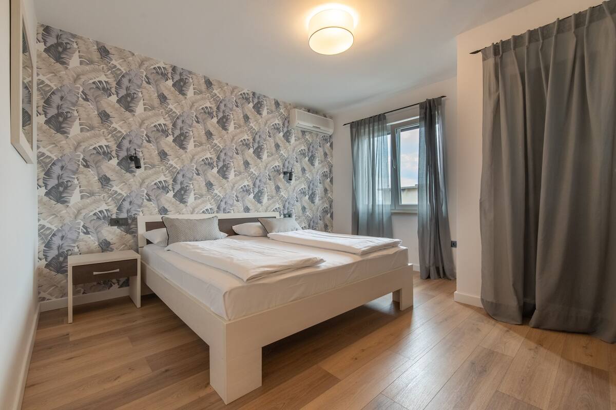 Un dormitorio con cama, mesita de noche y ventana con cortinas.