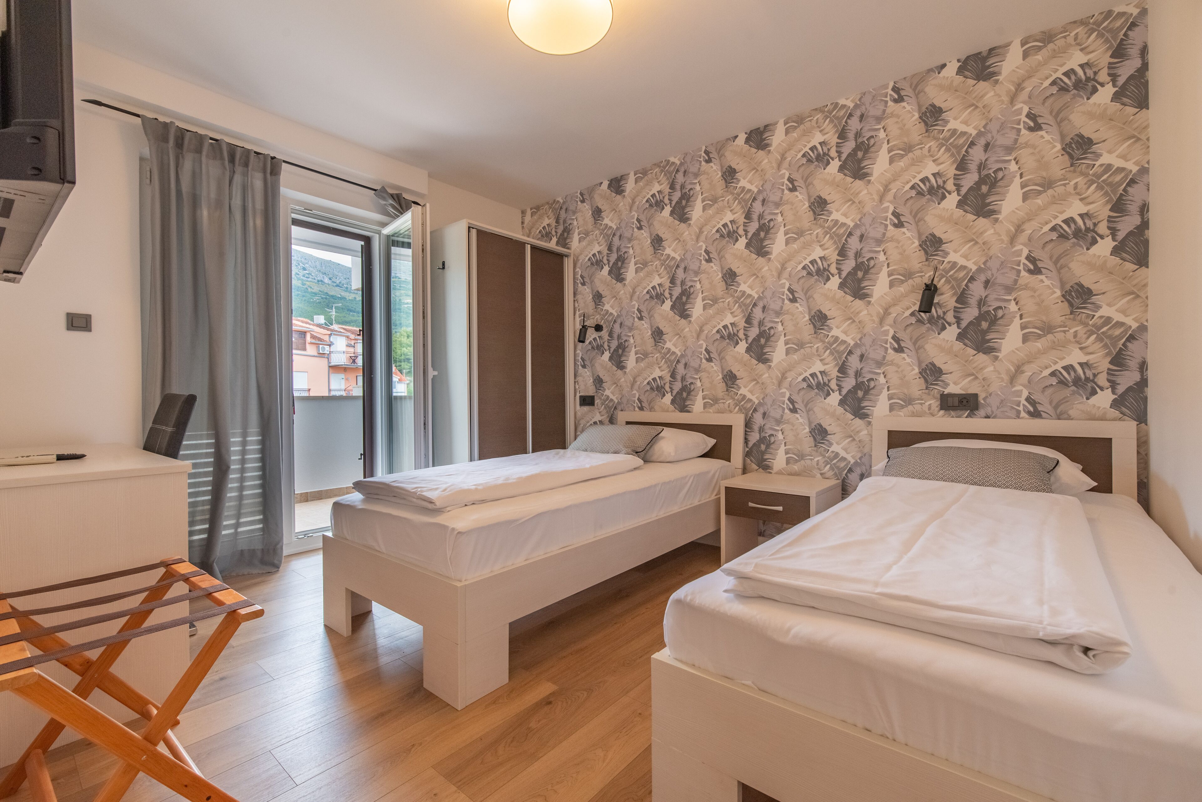 Une chambre d’hôtel avec deux lits, une chaise en bois, un bureau et une fenêtre avec des rideaux.
