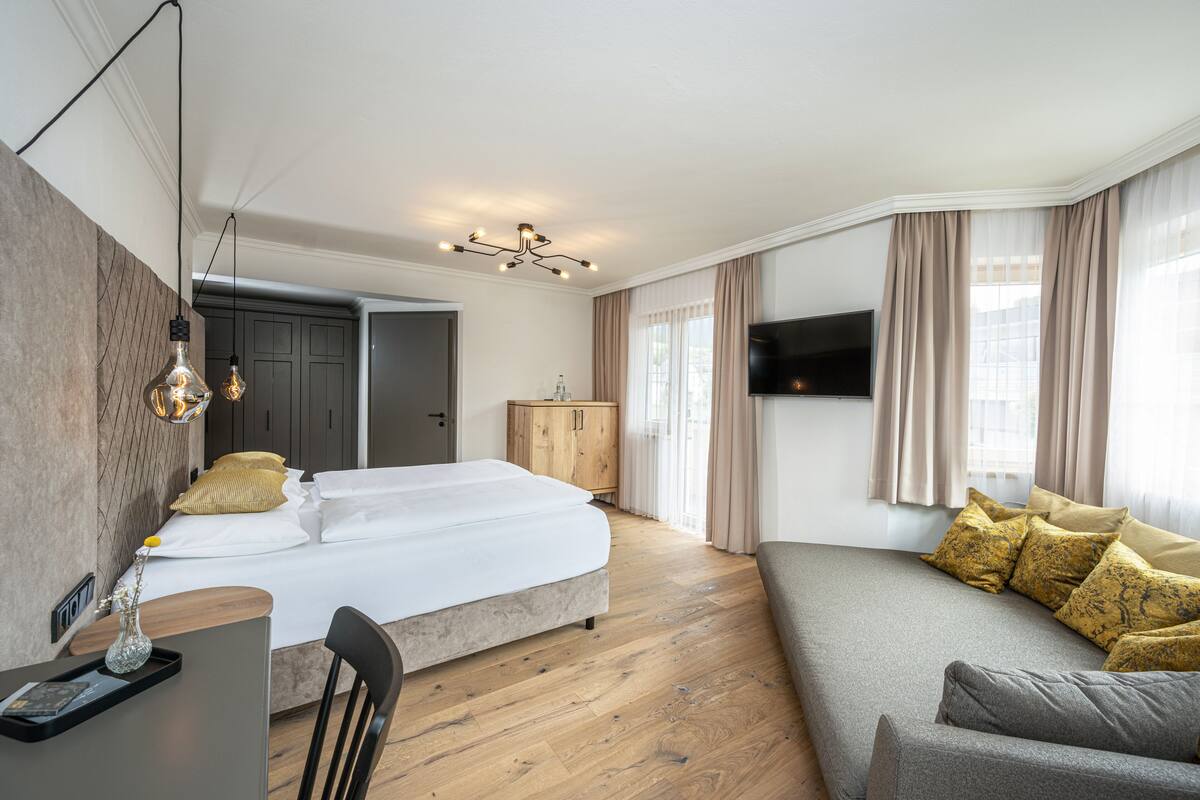 A hotel room with a bed, a sofa, a TV, and a desk with a chair.