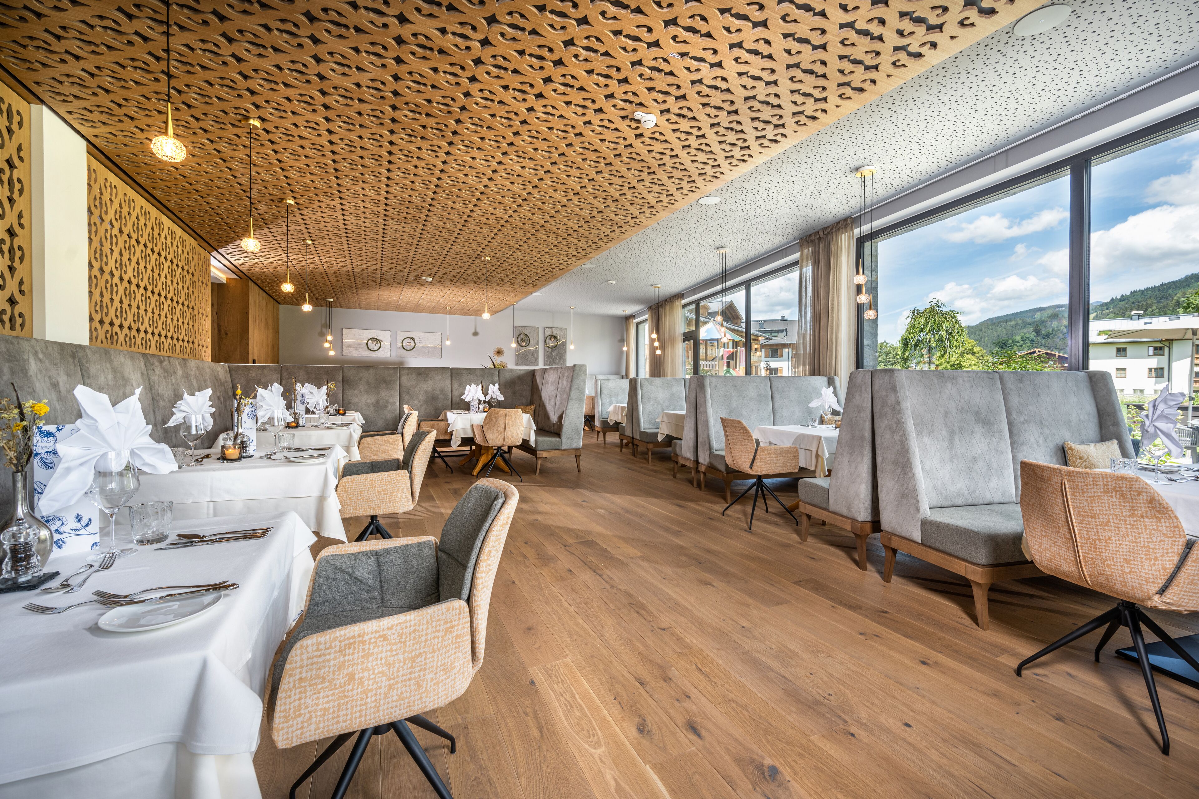 Un restaurante con suelo de madera, sillas tapizadas en gris y mesas dispuestas para comer.