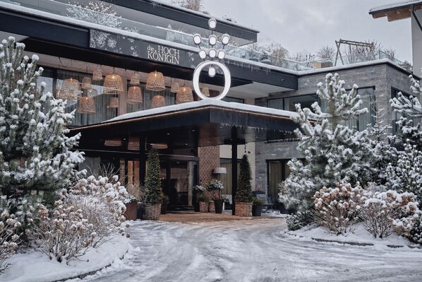 Une entrée d'hôtel moderne, avec un paysage enneigé, un logo circulaire bien visible et une allée couverte.