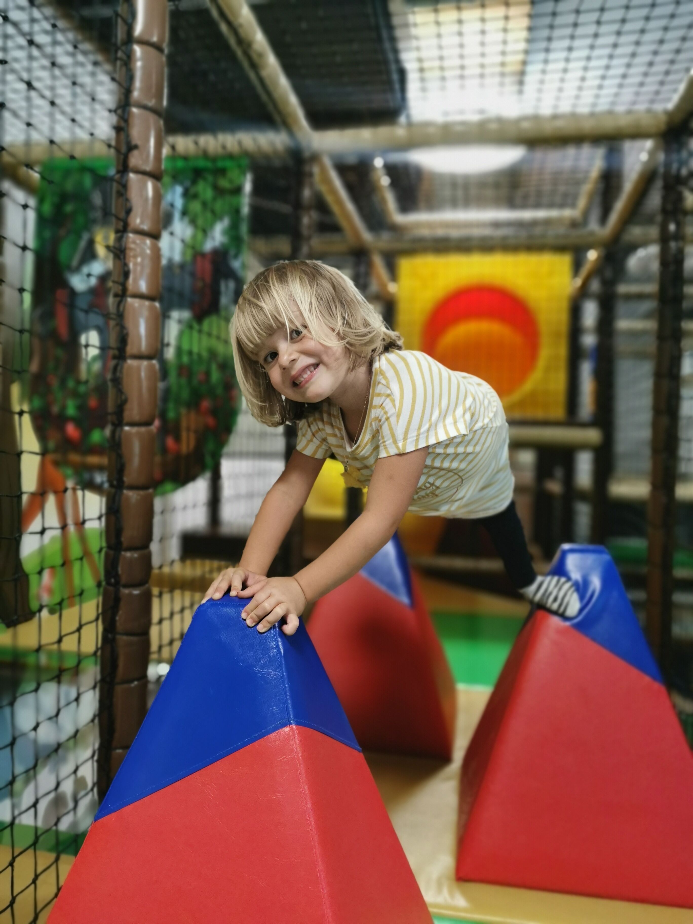 A child climbing over a colorful obstacle course in an indoor play area.