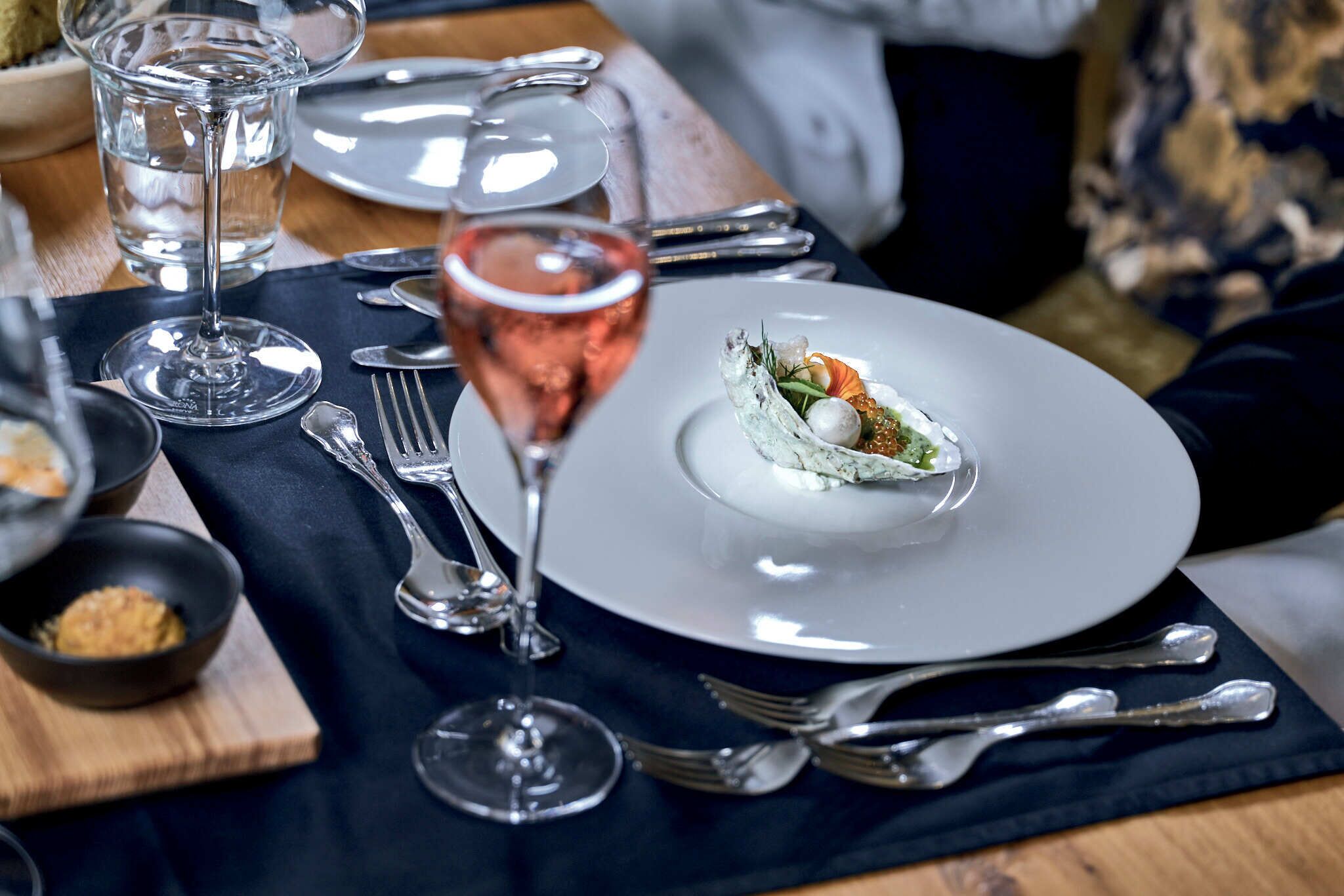 A dining table set with a white plate, a glass of rose wine, and silverware.