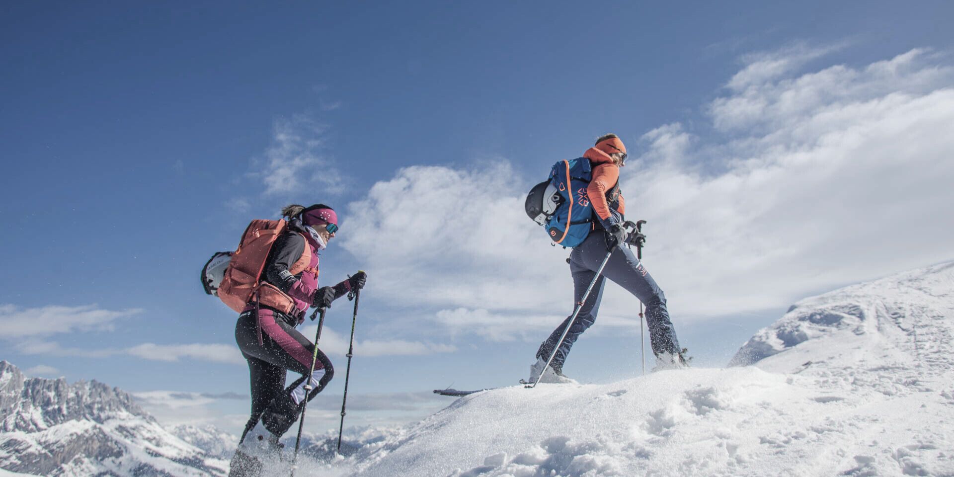 Deux randonneurs sur une montagne enneigée, sous un ciel dégagé.