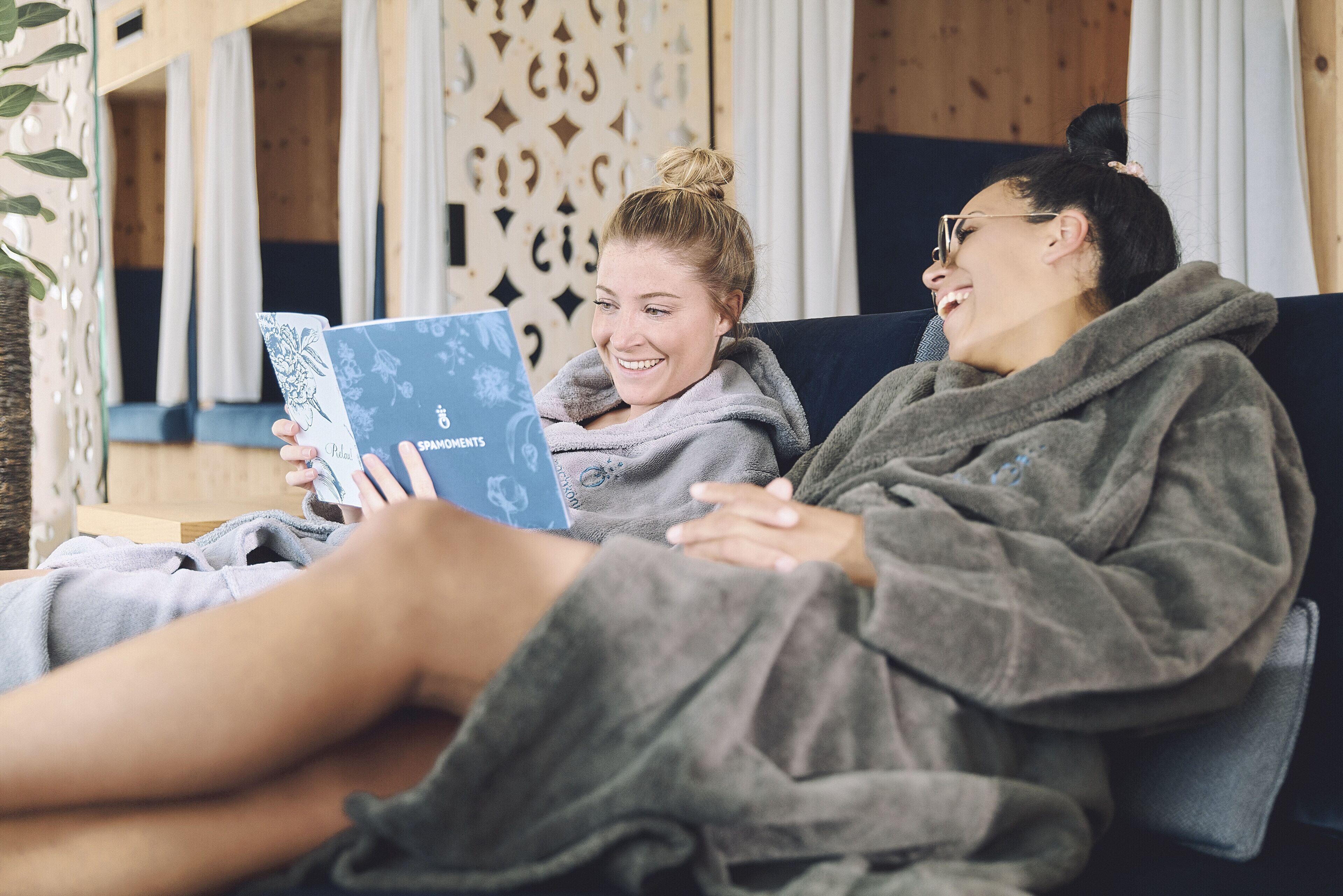 Two people sitting on a couch, one reading a book.