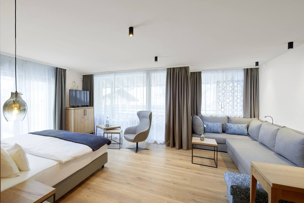 A modern hotel room with a bed, sofa, armchair, and a small table.