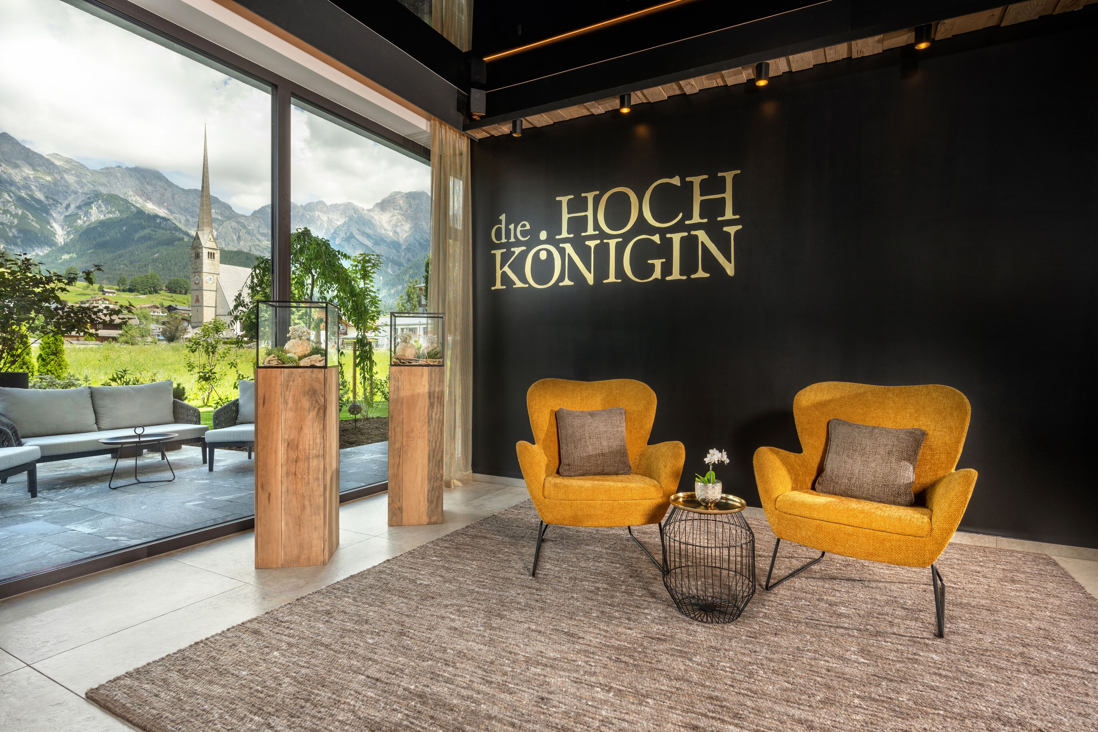 A modern interior with two yellow armchairs, a wooden pillar, and a view of mountains through large windows.