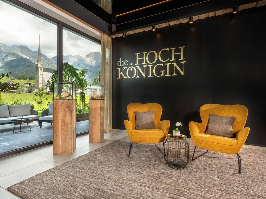 A modern interior with two yellow armchairs, a wooden pillar, and a view of mountains through large windows.