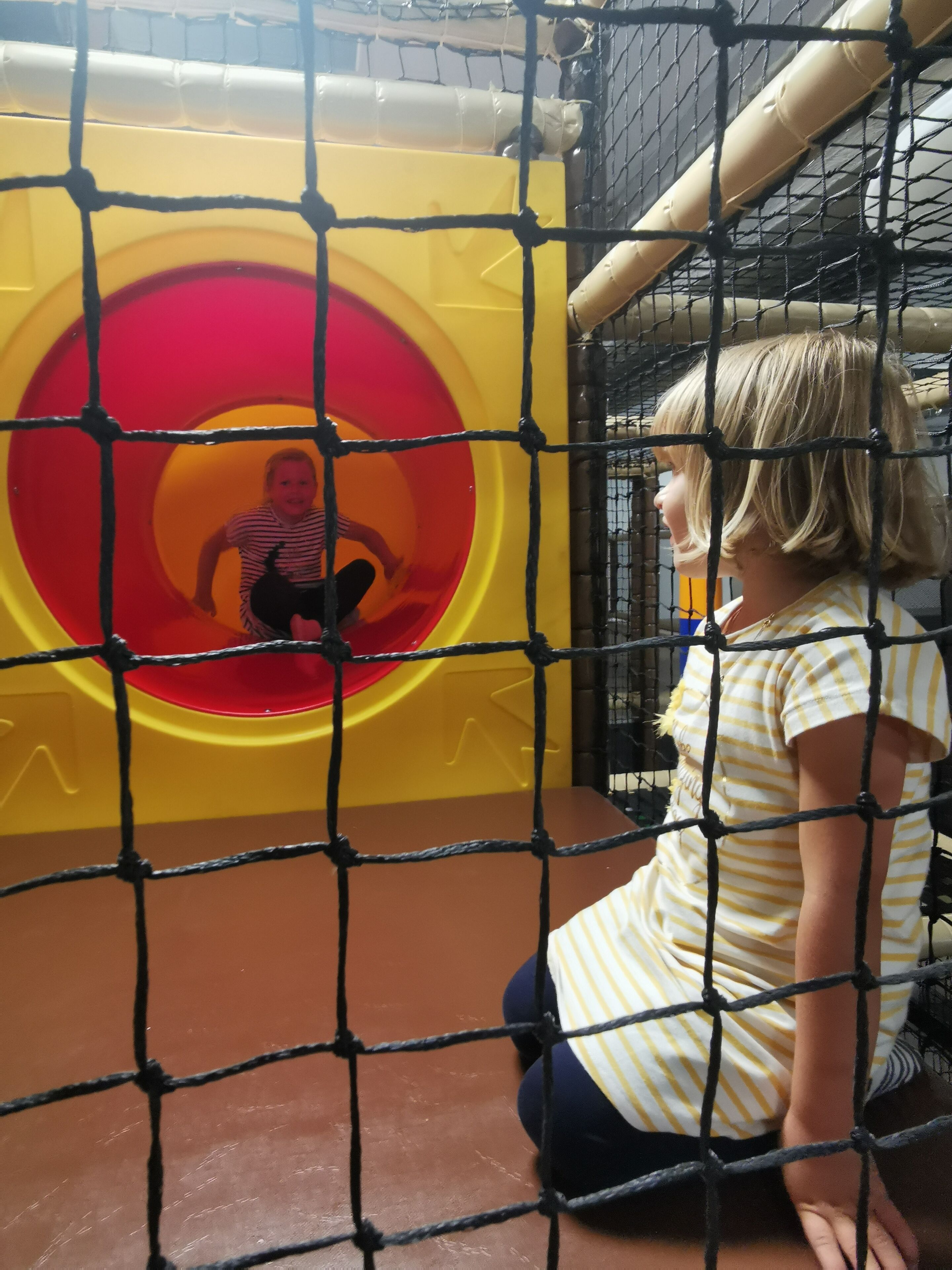 Ein Kind spielt auf einem Spielplatz mit einer Rutsche und einem Netz.
