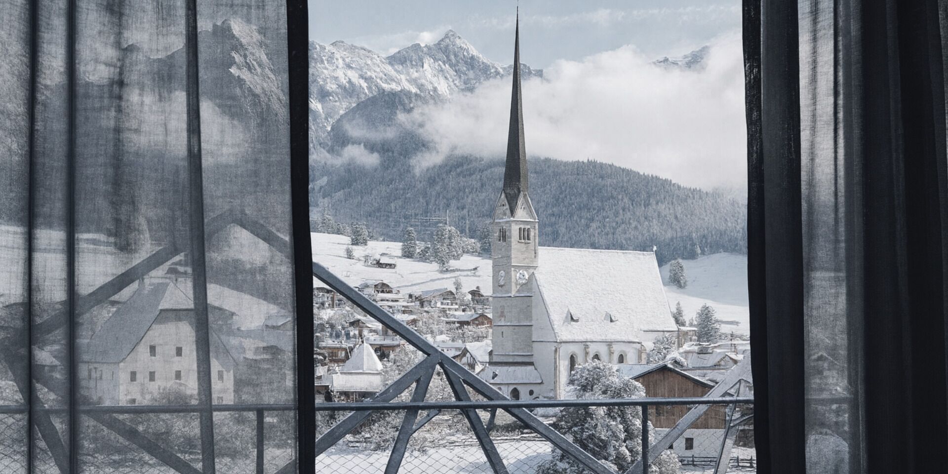 Un village enneigé, avec un clocher d’église imposant, entouré de montagnes et bordé d’une étendue d’eau.