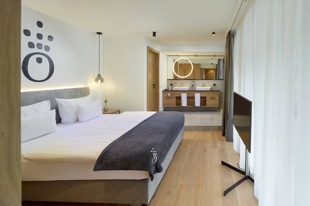 A modern hotel room with a large bed, bedside table, and a bathroom with a mirror and sink.