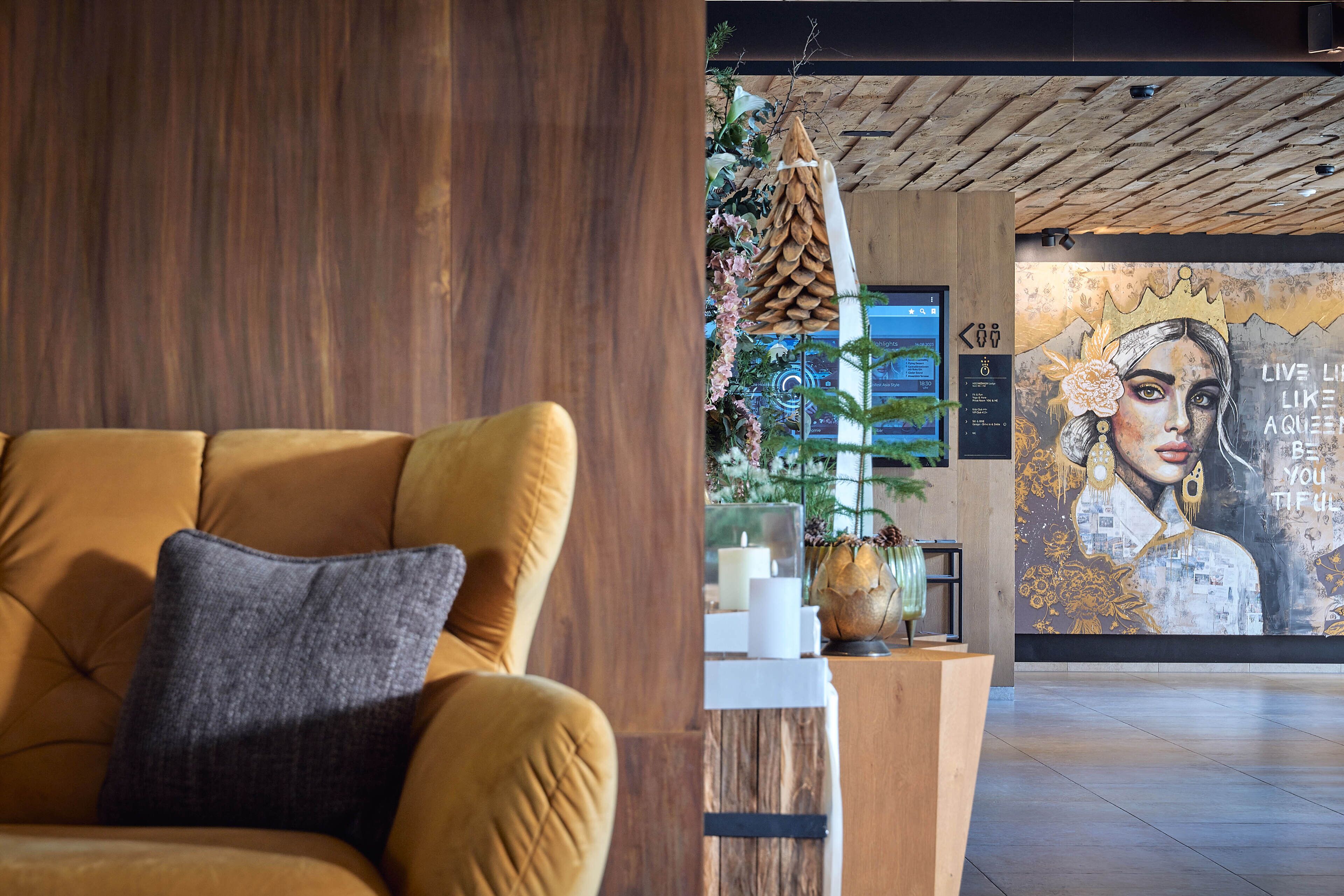 A modern lobby with a wooden reception desk, a large mural, and a comfortable seating area with a sofa and a decorative pillow.