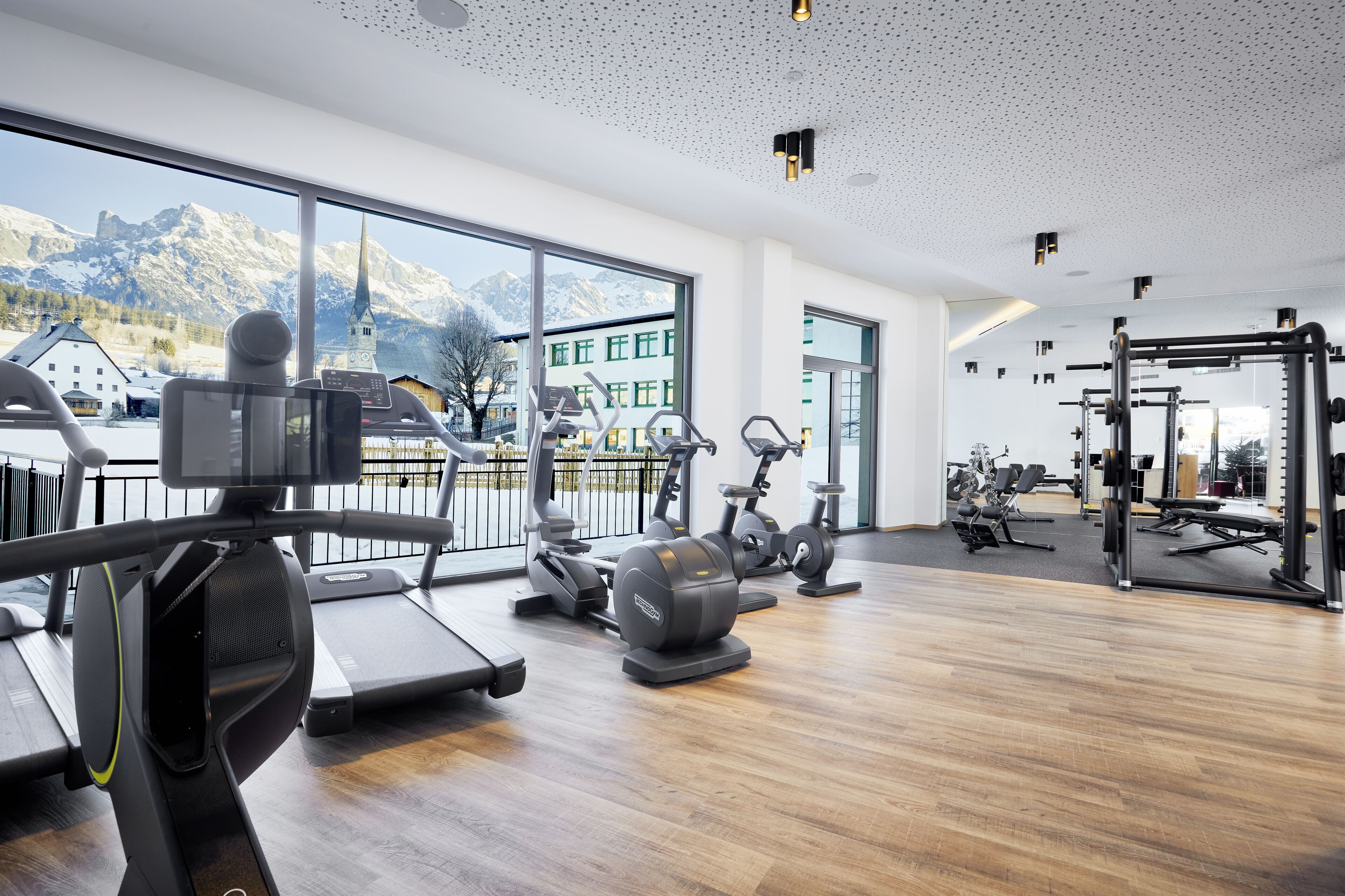 A gym with cardio machines, weightlifting equipment, and large windows offering a mountain view.