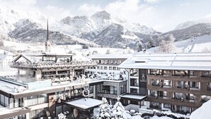 A modern hotel with a ski lift, snow-covered mountains, and a traditional building with a spire. - die Hochkönigin - Mountain Resort (Maria Alm am Steinernen Meer)