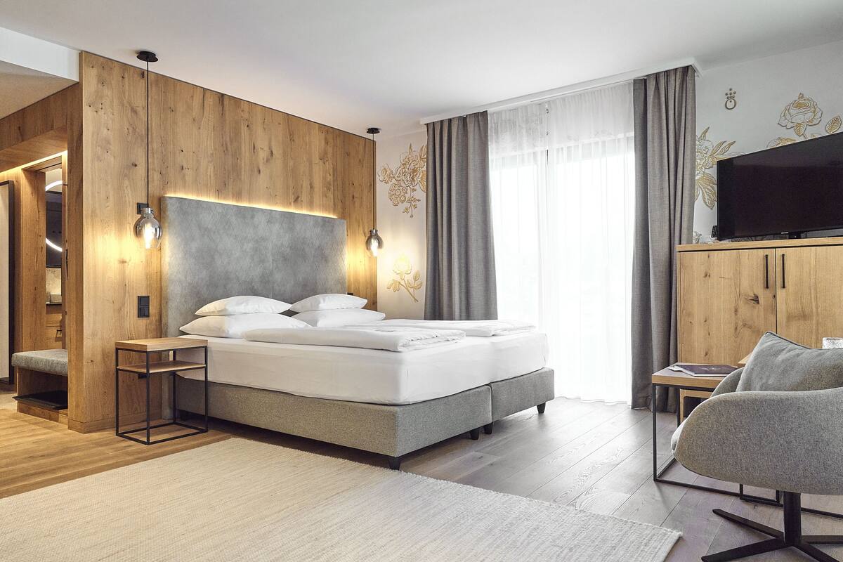 A modern bedroom with a large bed, a wooden wardrobe, a television, and a seating area.