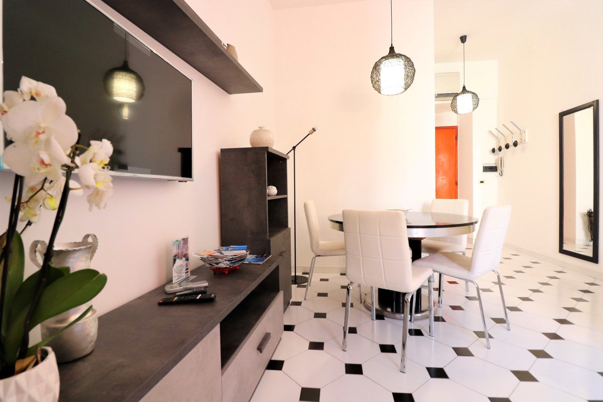 A modern dining area with a black and white checkered floor, a dark wooden console table with magazines and a remote control, and a white dining set.