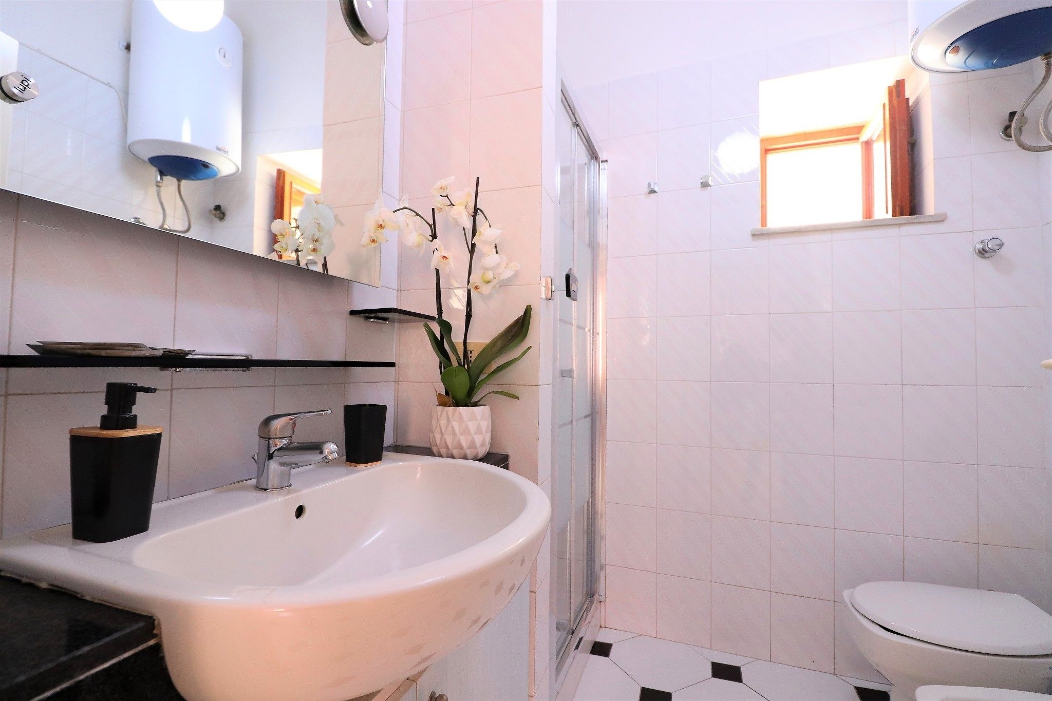 A modern bathroom with a freestanding sink, a toilet, a shower enclosure, and a small window.