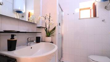 A modern bathroom with a freestanding sink, a toilet, a shower enclosure, and a small window.