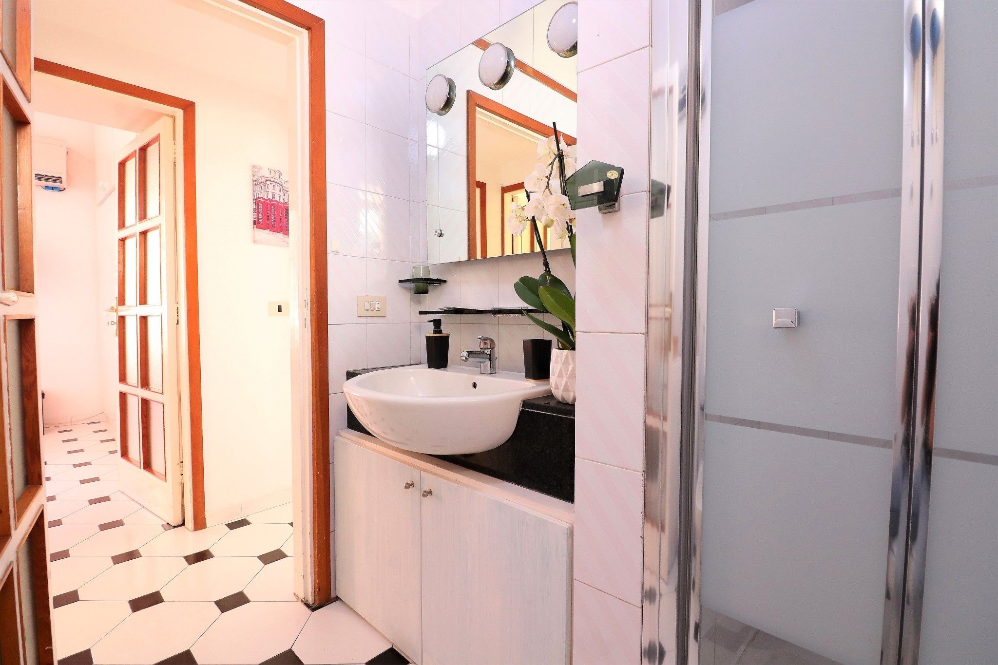 Un baño con lavamanos blanco, un espejo y una orquídea en maceta.