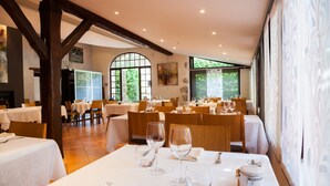 Comedor con mesas dispuestas para una comida, vigas de madera en el techo y ventanas amplias que dejan entrar luz natural.